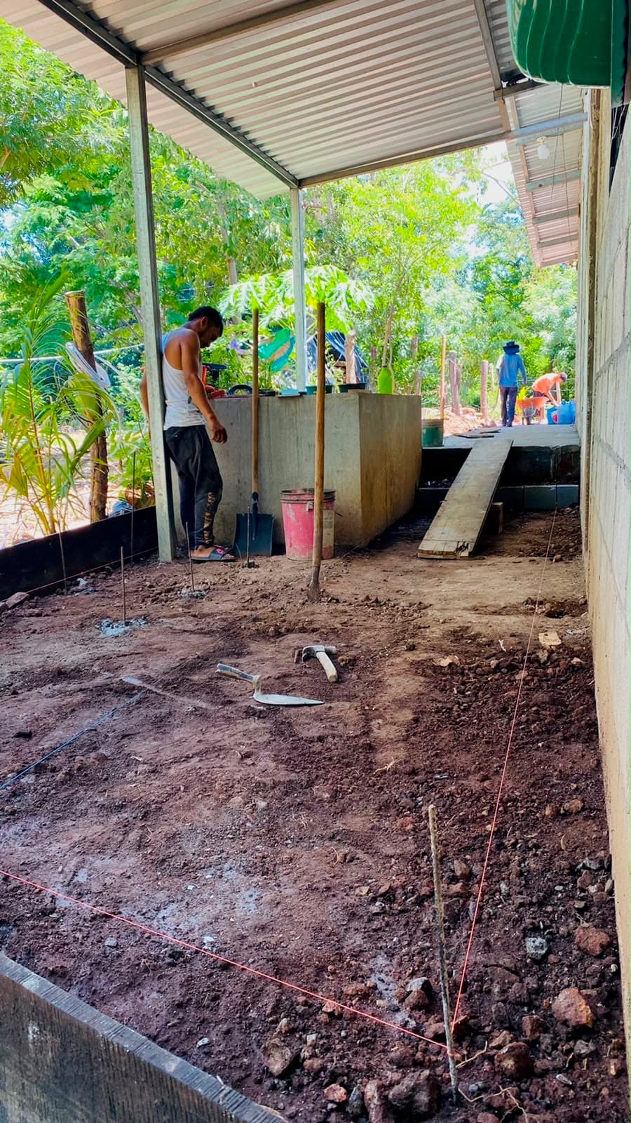Un trabajador preparando el terreno para un nuevo piso de concreto junto a una vivienda